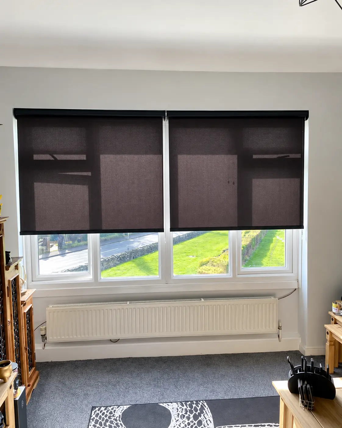 Dark roller blinds fitted across a wide window in a Bradford home